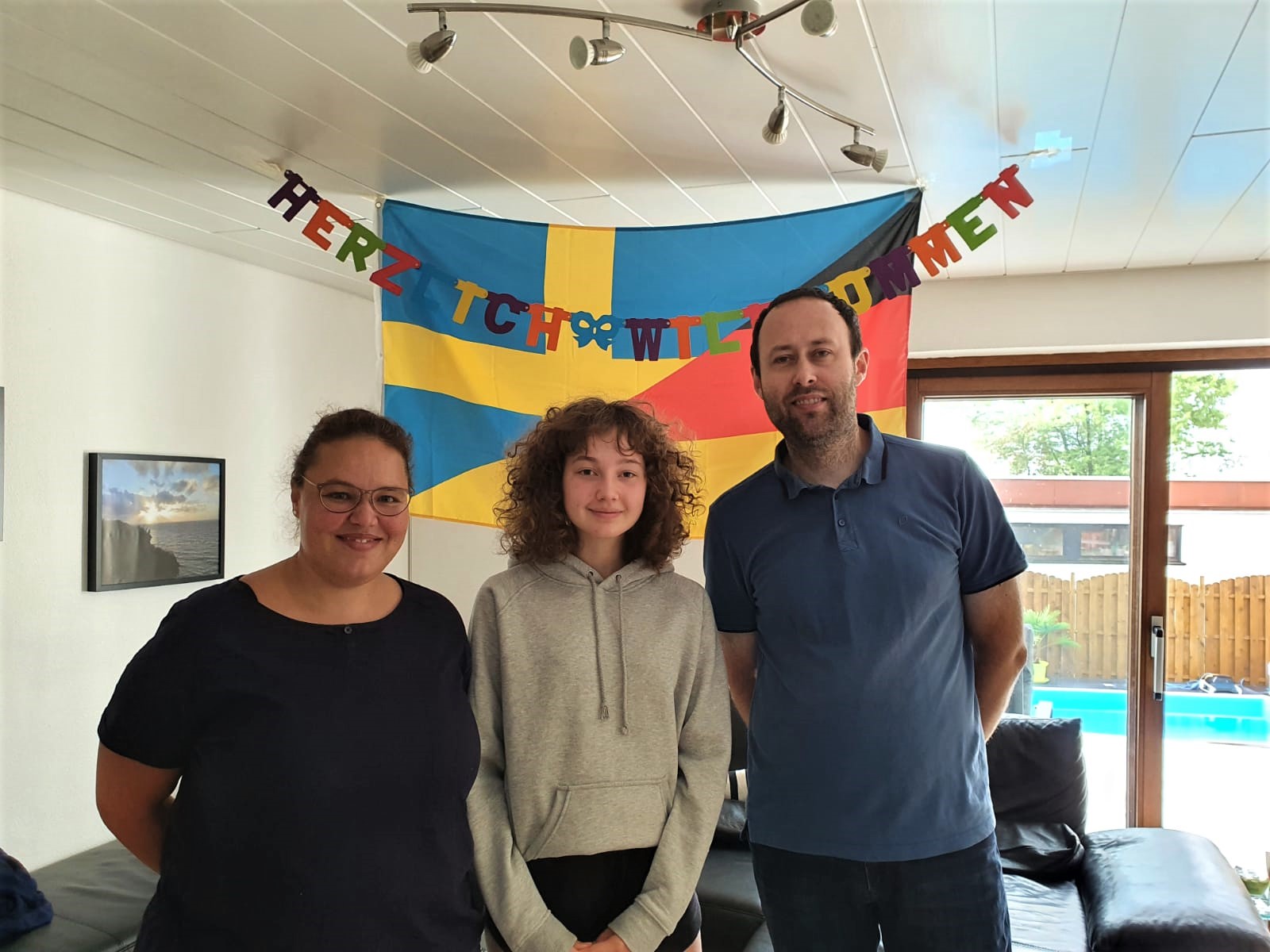 Deutsche Gastfamilie mit schwedischem Gastkind vor einer Deutschland-Schweden Flagge und Herzlich Willkommen - Girlande