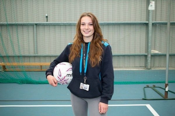 Austauschschülerin trägt einen Volleyball im Arm in einer Sporthalle