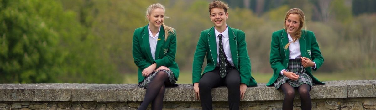 High School Schüler und Schülerinnen in grüner Schuluniform sitzen auf einer Mauer