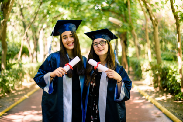 High School Absolventinnen mit Umhang und Zeugnis im Wald in den USA