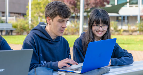 High School Schüler und Schülerin arbeiten draußen an einem Laptop