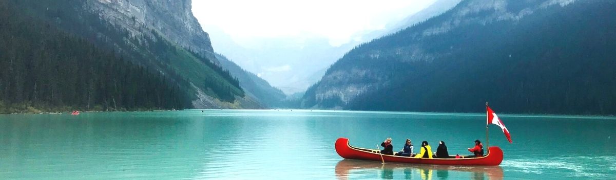 Austauschschüler und Schülerinnen fahren in einem Kanu auf einem See zwischen Bergen in Kanada