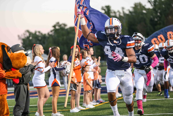 High School Football Spieler rennen auf das Spielfeld und werden von Cheerleadern angefeuert