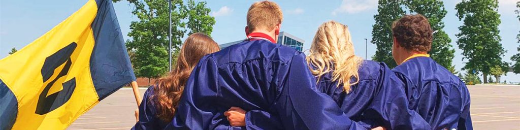 High School Schülerinnen und Schüler in ihrem Absolventenoutfit sind mit dem Rücken zur Kamera gedreht