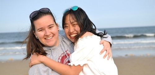 Zwei Austauschschülerinnen umarmen sich am Meer