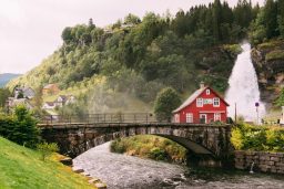 Rotes Haus mit Wasserfall und Brücke in Norwegen