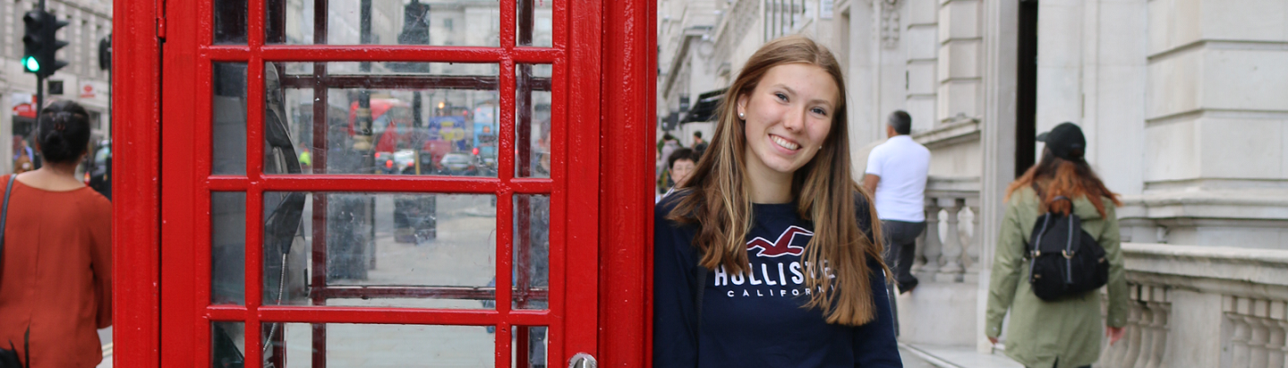 Austauschschülerin in London neben einer roten Telefonzelle